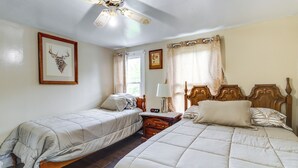 Un dormitorio con dos camas individuales, cabecero de madera, mesita de noche con lámpara, cuadro con ciervo enmarco y ventana con cortinas.