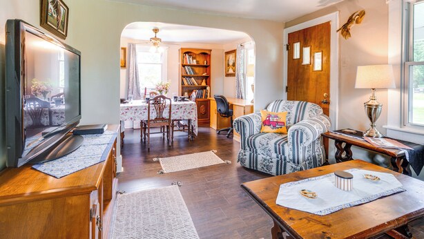 Una sala de estar con televisor, un sofá, una mesa de comedor con sillas y una estantería.
