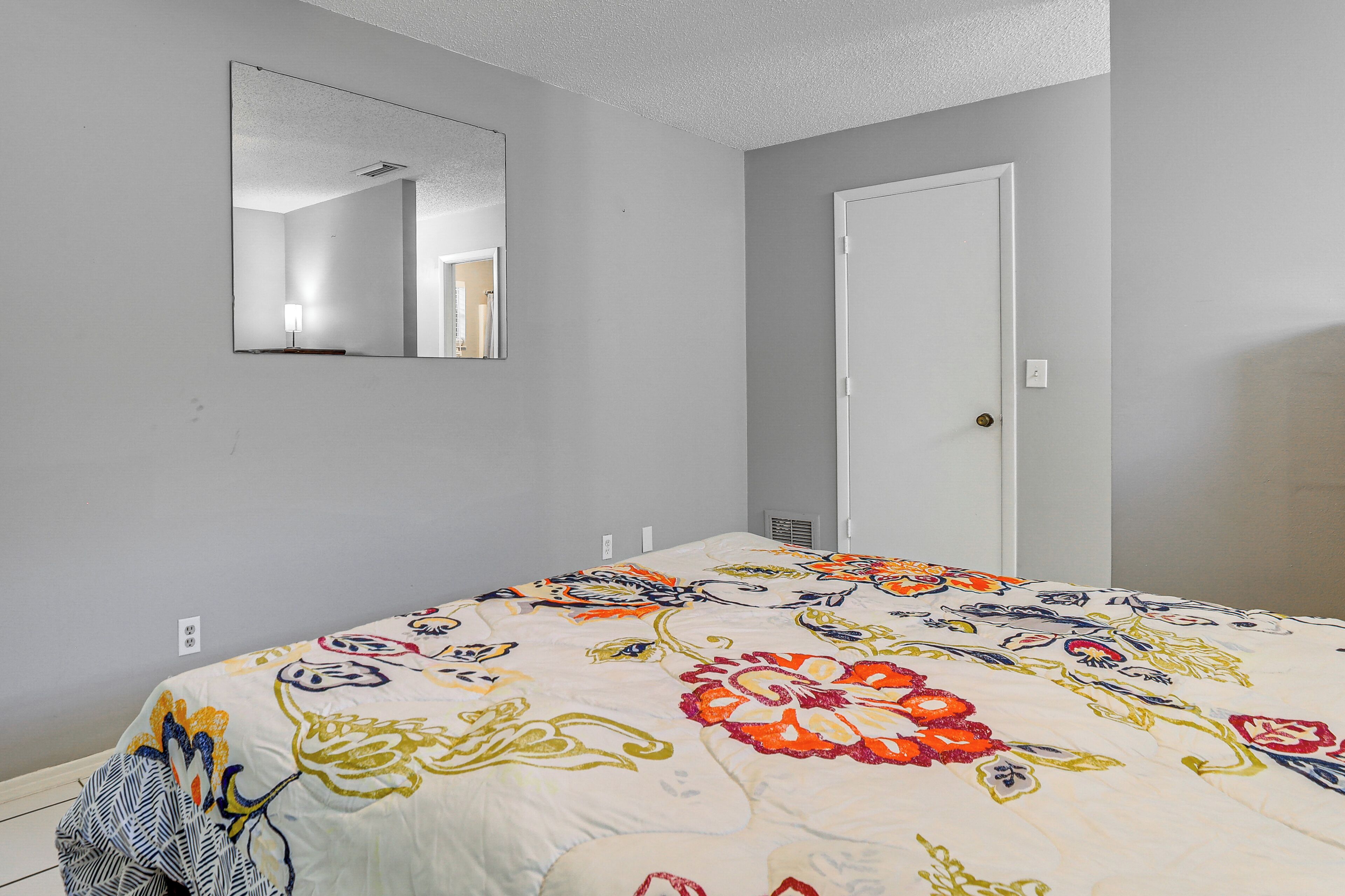 A bedroom with a bed, a mirror, a door, and a light switch on the wall.