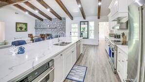 A spacious kitchen with a large island, white cabinetry, and stainless steel appliances. There is a stone accent wall and a view into the dining area. - Lake Hamilton Views: Hot Springs Family Home! (Hot Springs)