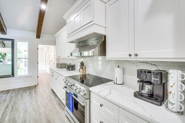 A modern kitchen with white cabinetry, a stainless steel range hood, a Keurig coffee maker, and a marble countertop. - Lake Hamilton Views: Hot Springs Family Home! (Hot Springs)