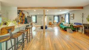A spacious living area with a wooden floor, a green sofa, and a kitchen area with wooden beams. - Walk to Putnam Lake: Updated Home w/ Deck (Patterson)