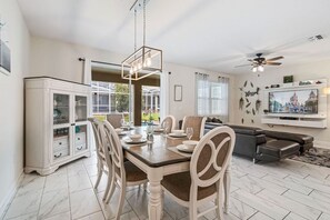 A dining area with a table set for four, a cabinet with glass doors, a ceiling fan, and a television mounted on the wall.