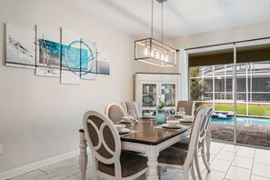 A dining area with a table set for four, a chandelier, and a view of a swimming pool through a glass door.