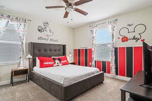 A bedroom with a bed, a nightstand, a ceiling fan, and Mickey Mouse-themed decor.