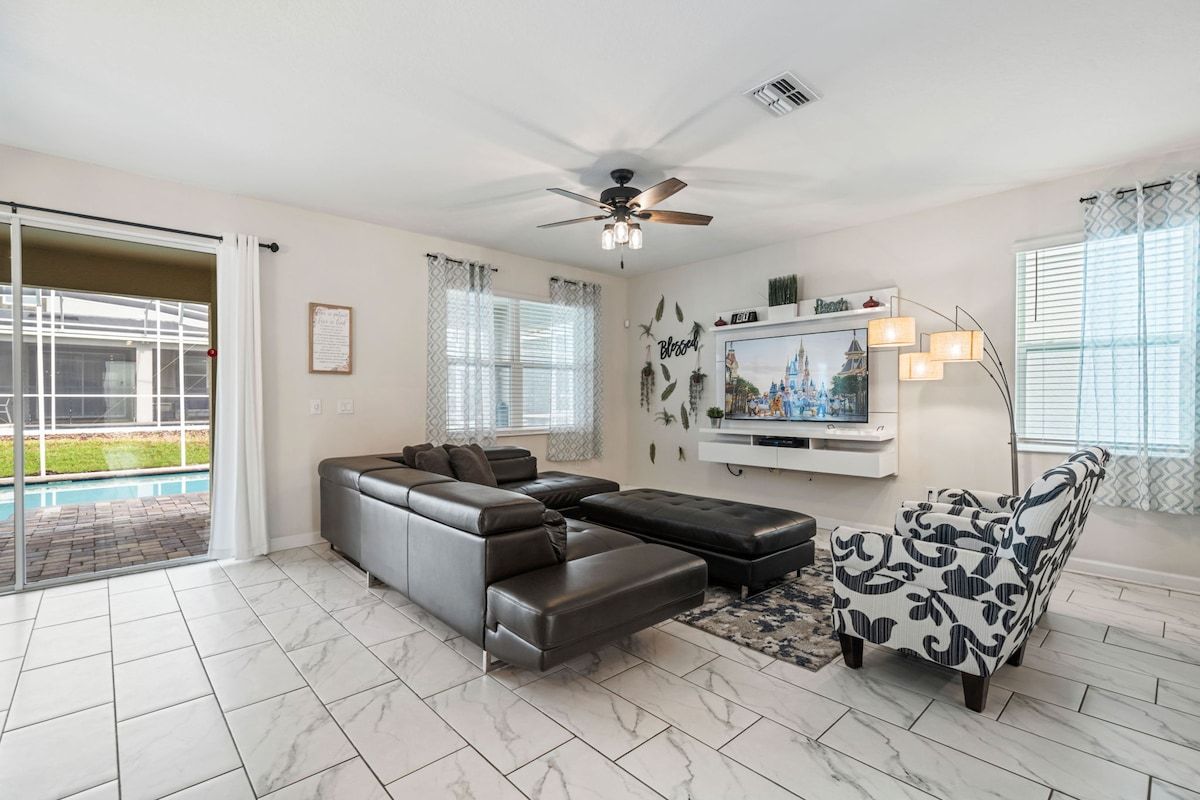 A modern living room with a sectional sofa, a flat-screen TV, and a ceiling fan.