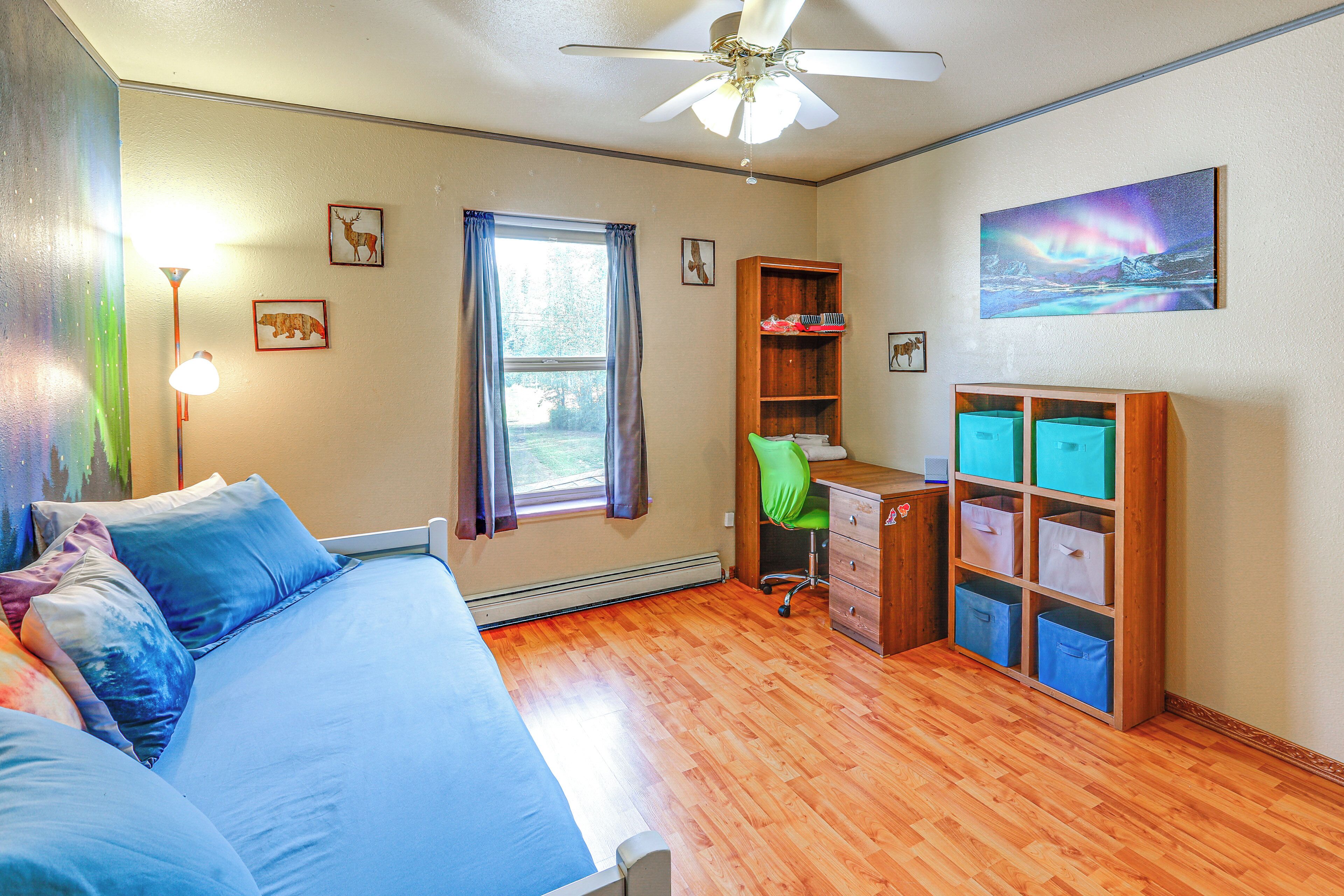 A bedroom with a bed, desk, chair, and storage units.