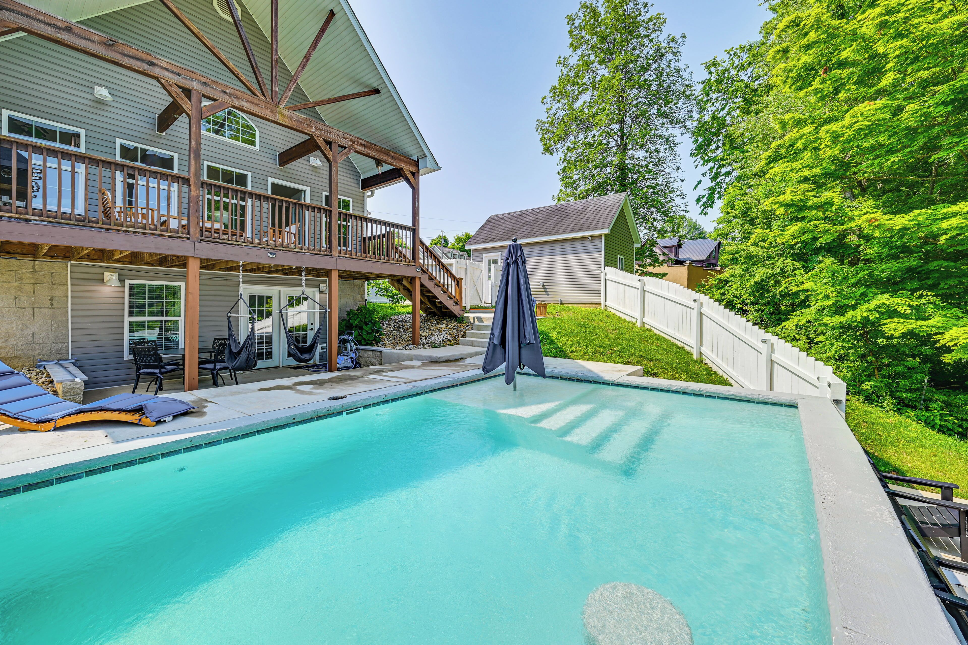 A backyard with a swimming pool, a covered patio, and a wooden deck.