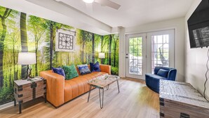 A living room with a forest mural, an orange sofa, a blue armchair, a wooden coffee table, and a ceiling fan. - Pool, Lake Views, Dock & More: Mt Vernon Getaway (Mount Vernon)