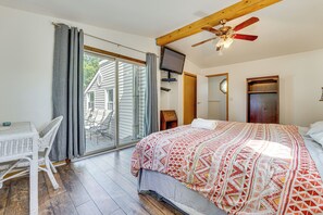 Une chambre dotée d’un grand lit, d’une télévision, d’un ventilateur de plafond et d’une porte-fenêtre coulissante donnant sur un balcon.