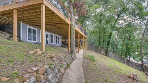 A wooden deck with a stone pathway leading to a building with large windows and a covered area. - Lake Hamilton Views: Hot Springs Family Home! (Hot Springs)