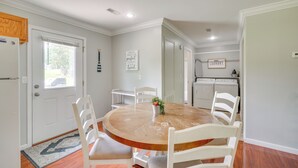 Een eetgedeelte met een ronde houten tafel, witte stoelen en een keuken op de achtergrond.