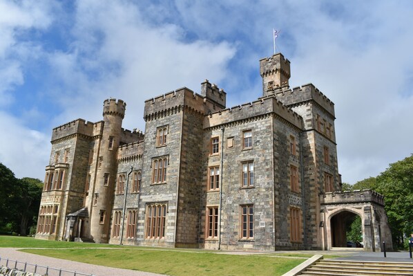 A large, historic stone building with multiple towers and arched windows, likely a castle or manor house. - Arnisdale House (Isle of Lewis)
