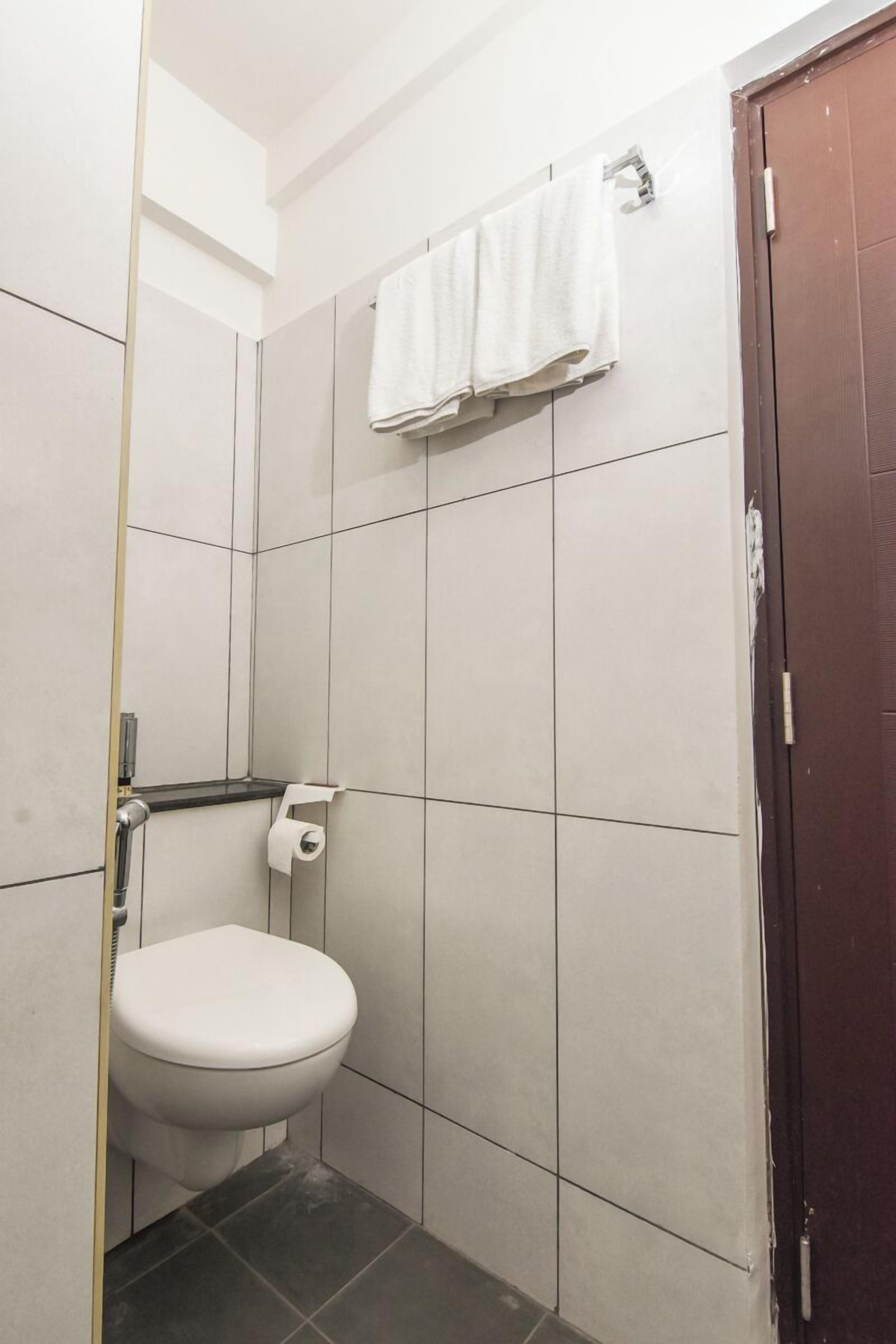 Une petite salle de bain carrelée, avec des toilettes, une serviette accrochée au mur et une porte.