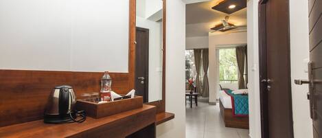 A hotel bathroom with a wooden vanity, a mirror, a kettle, and a bottle of water.