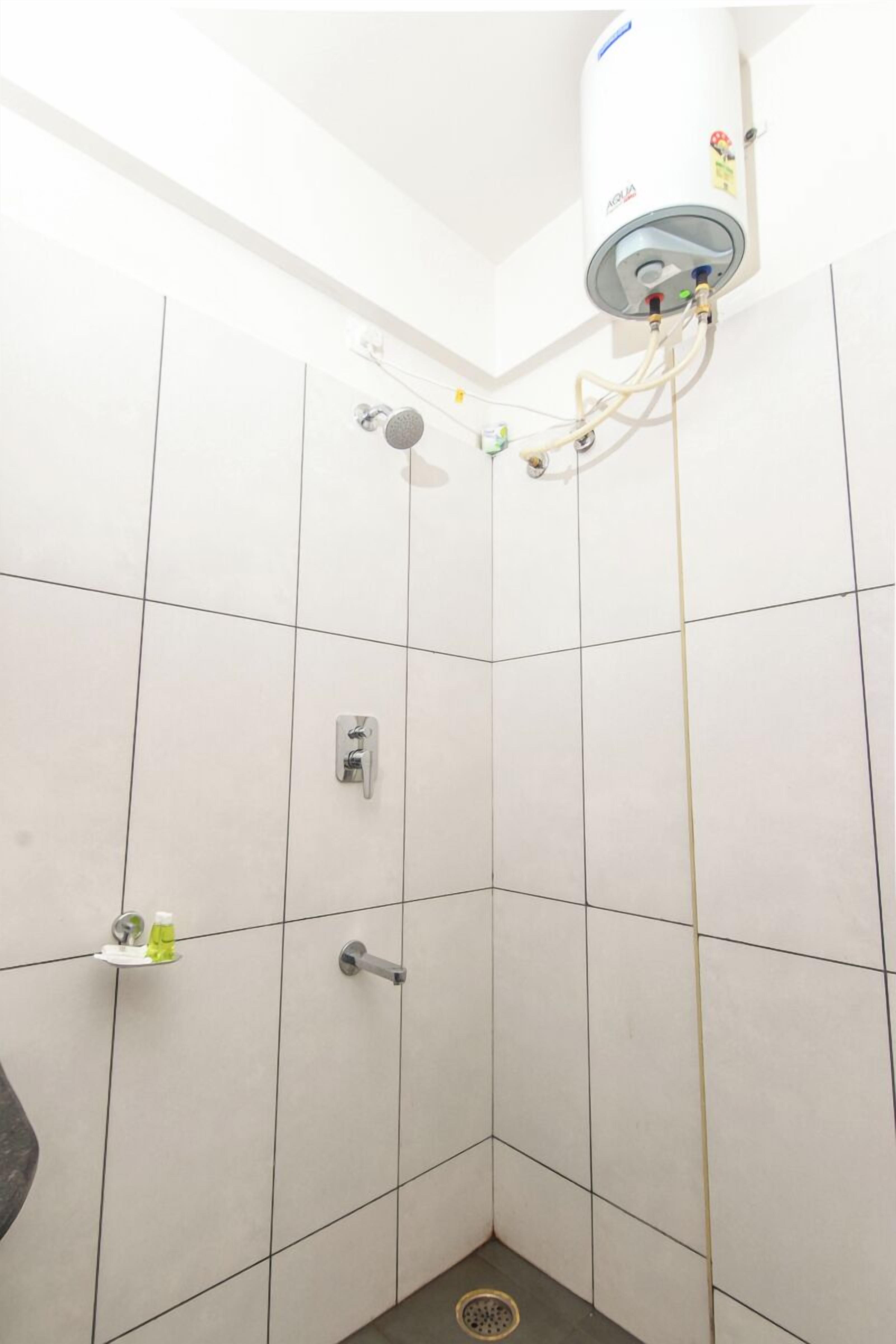 Eine Eckdusche mit weißen Fliesen, einem Warmwasserbereiter und einem Händetrockner.
