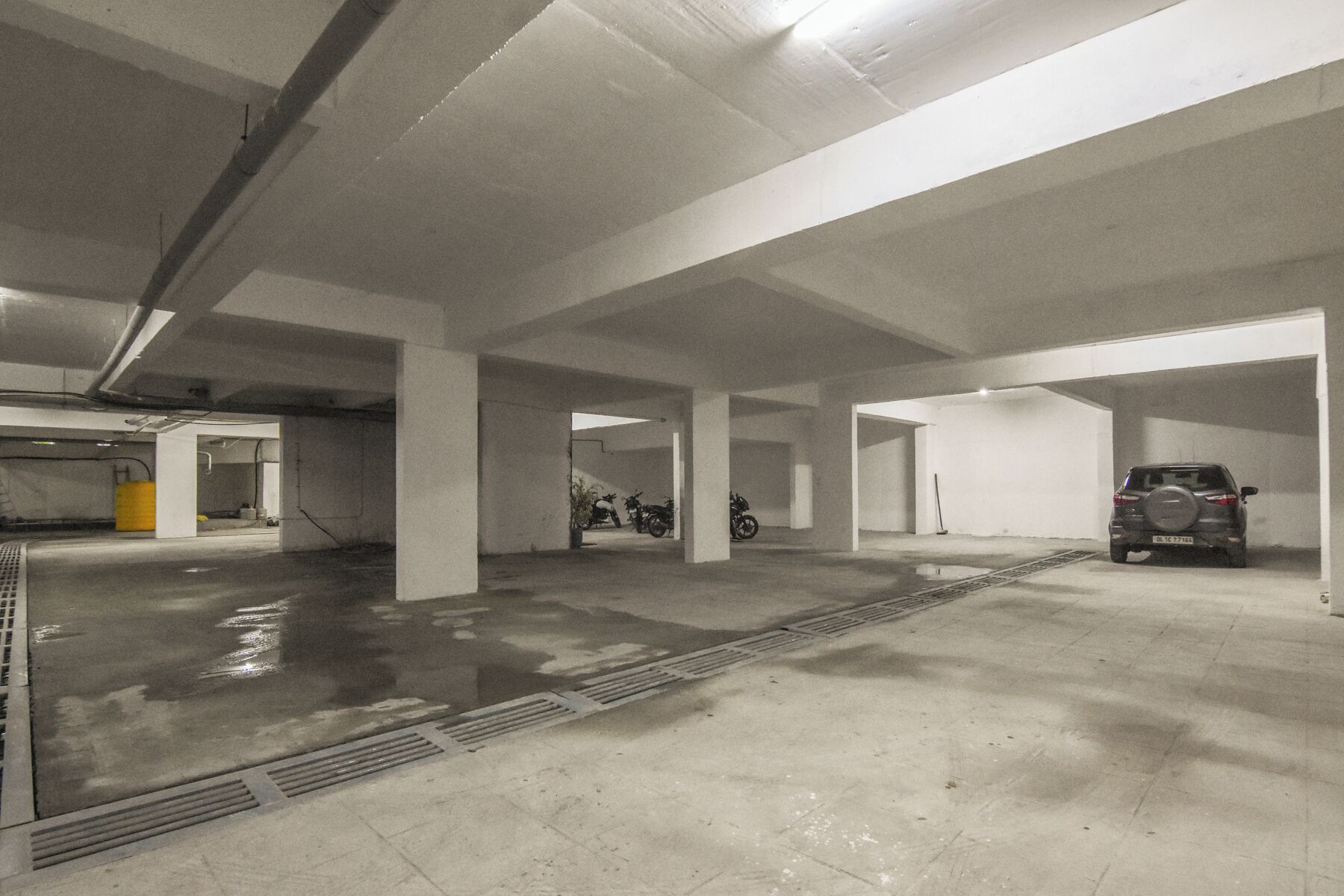 An underground parking garage with concrete pillars, a wet floor, and a few parked vehicles.