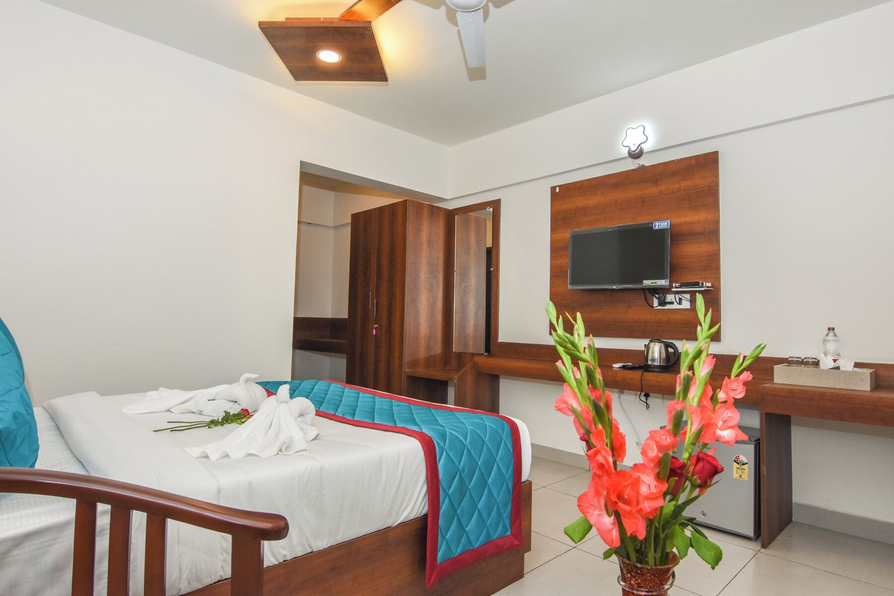 A hotel room with a bed, a desk, a television, and a vase of flowers.