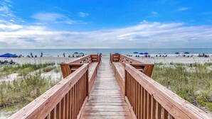 Une promenade en bois menant à une plage où se trouvent des parasols et des gens.