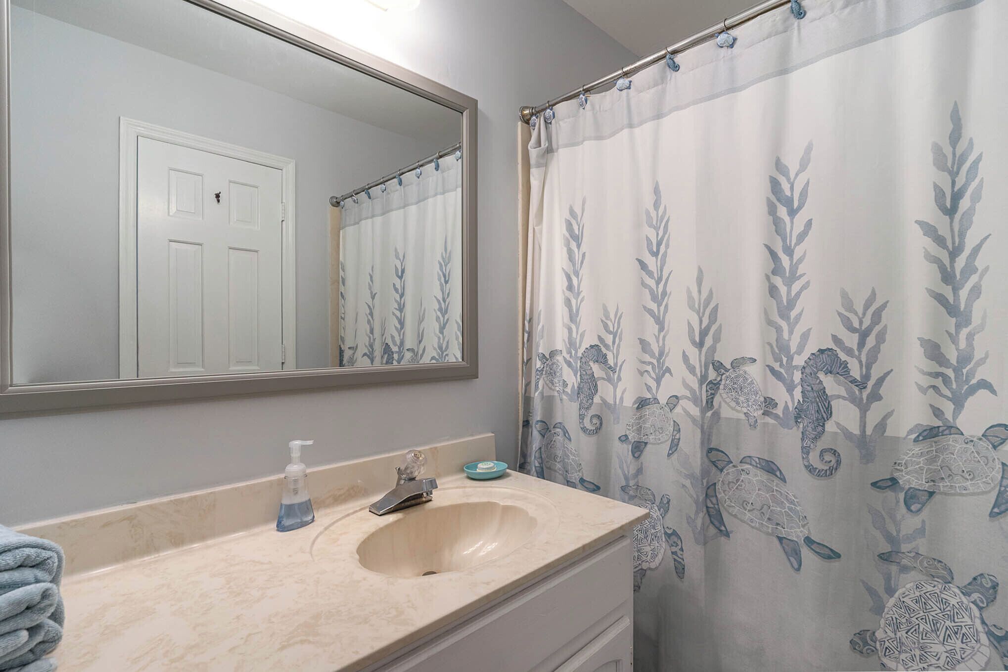 A bathroom with a sink, mirror, and shower curtain with a sea turtle pattern.
