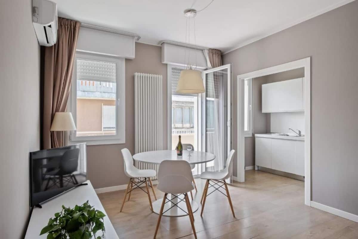 Ein modernes Wohnzimmer mit einem runden Esstisch, weißen Stühlen, einem Flachbildfernseher und einem Blumentopf.