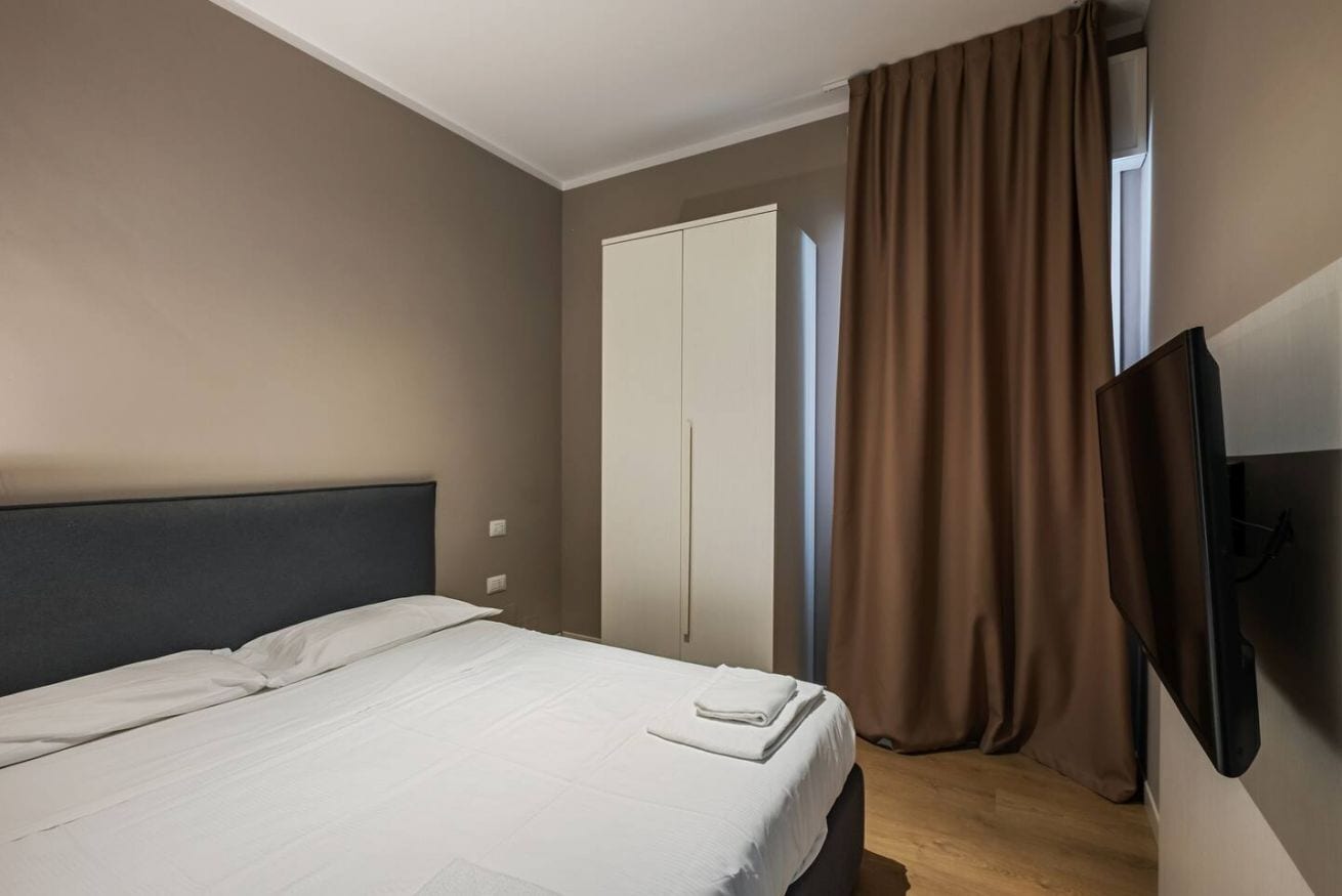 A hotel room with a bed, a wardrobe, a television, and a window with curtains.