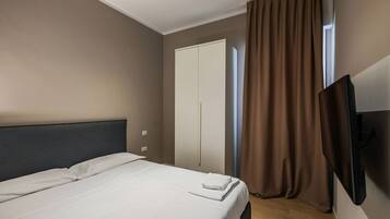 A hotel room with a bed, a wardrobe, a television, and a window with curtains.