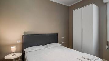 Et hotelværelse med seng, natbord med lampe og et klædeskab.