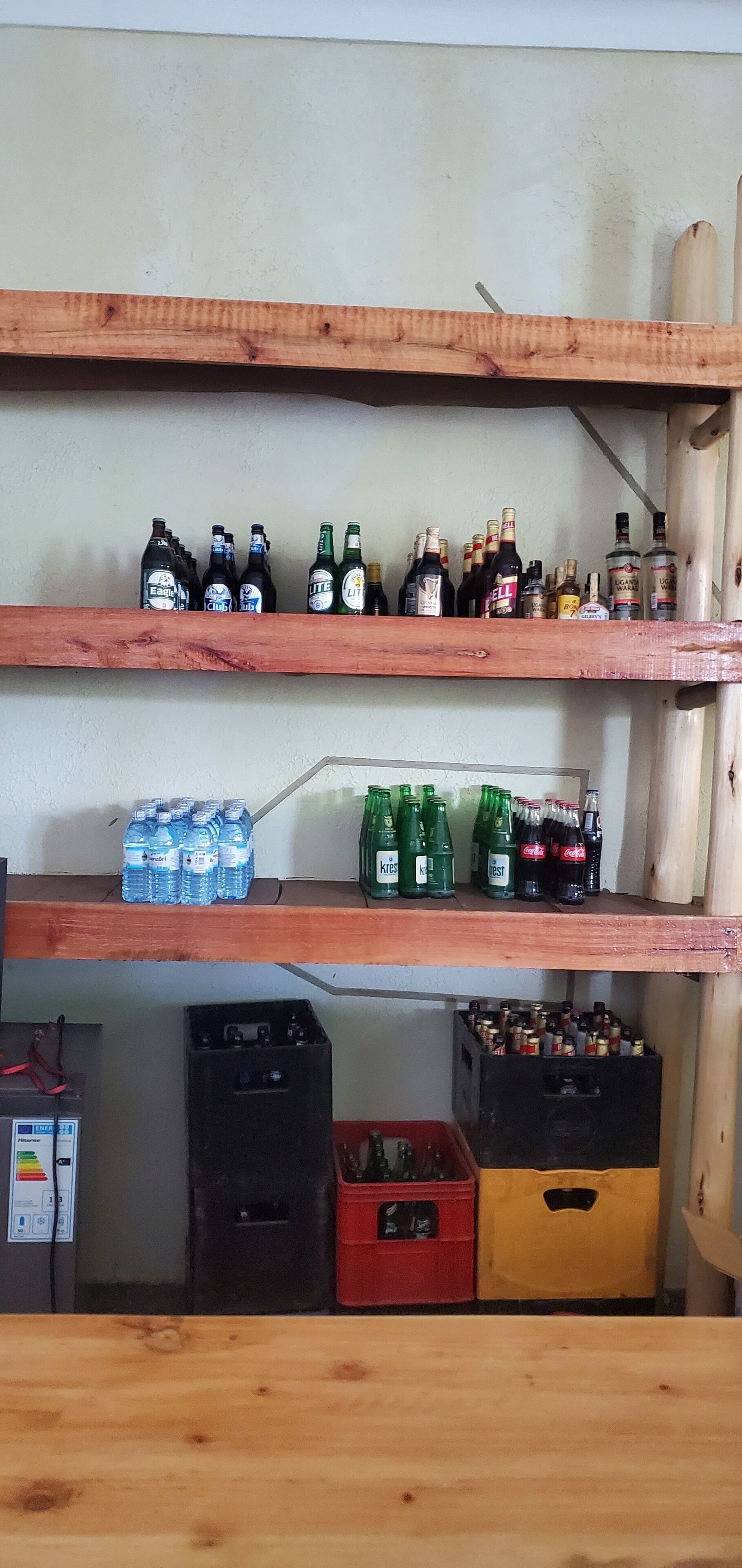 A shelf with various bottles, including beer and soda, and two crates below.