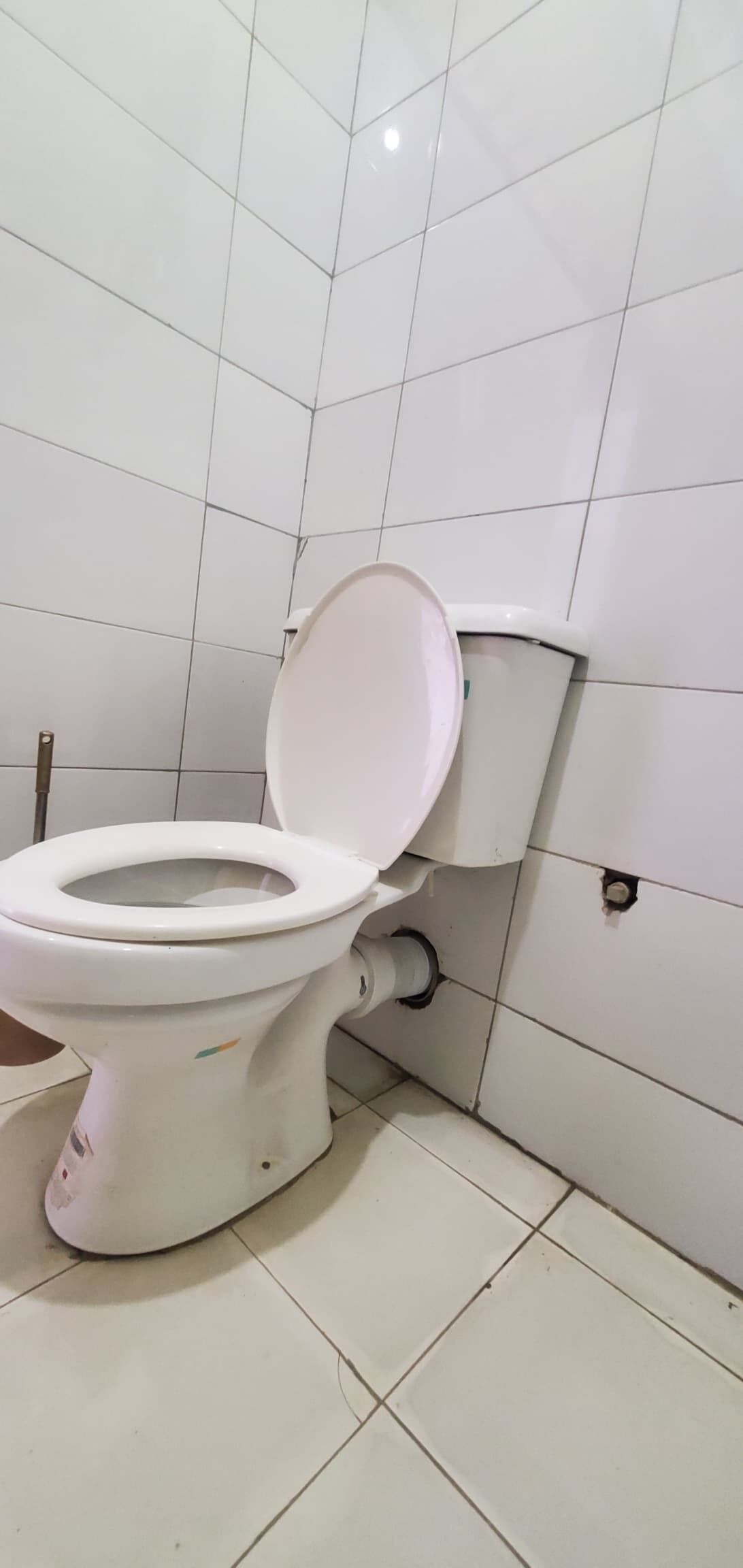 A toilet with a white tank and lid, positioned against a tiled wall.