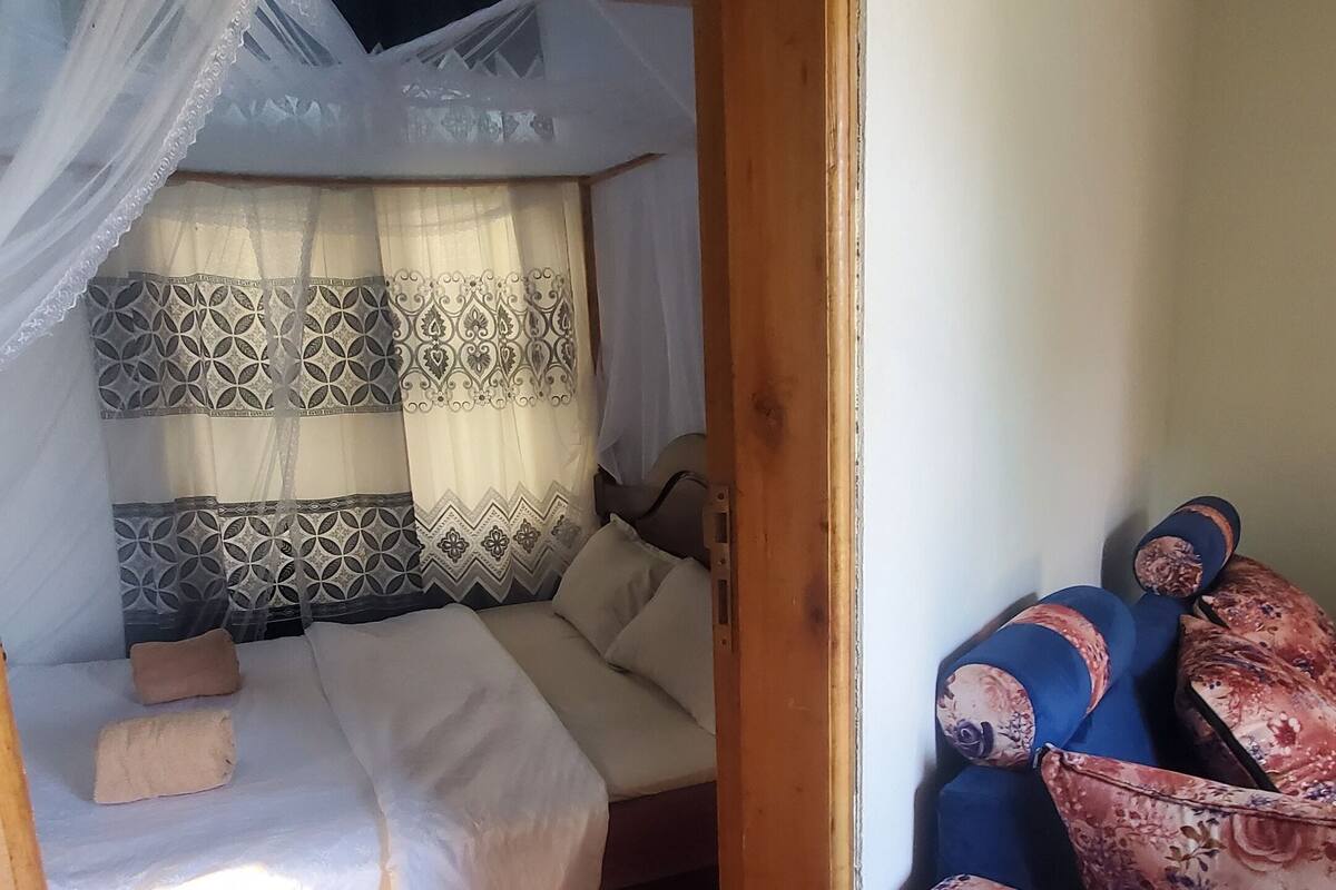 A room with a bed under a mosquito net, a wooden floor, and a sofa with patterned cushions.