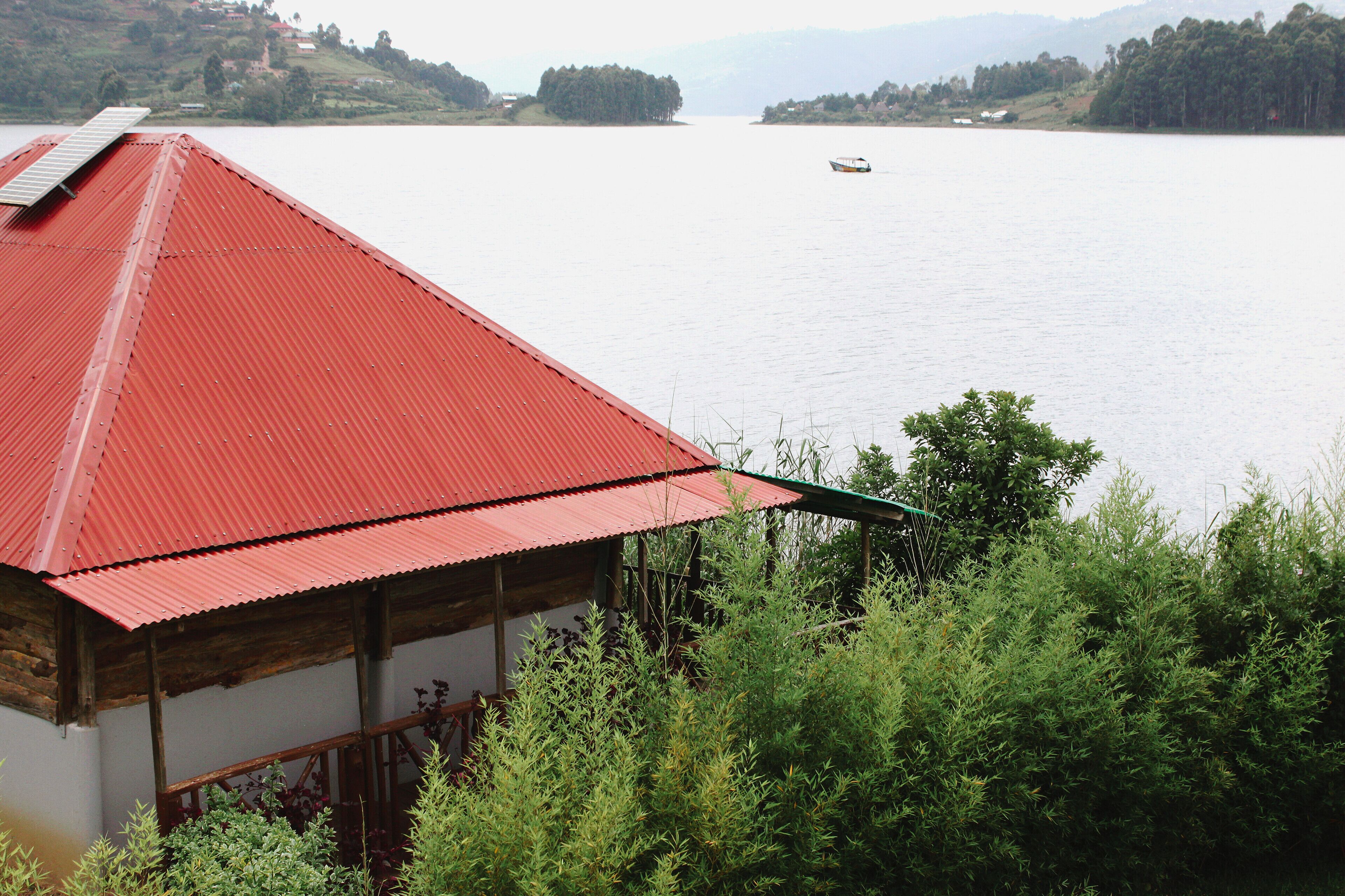 A building with a red roof overlooking a calm lake with a boat in the distance.