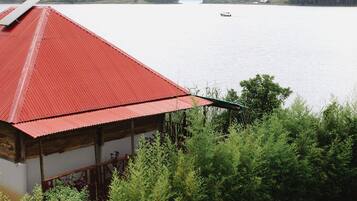 A building with a red roof overlooking a calm lake with a boat in the distance.