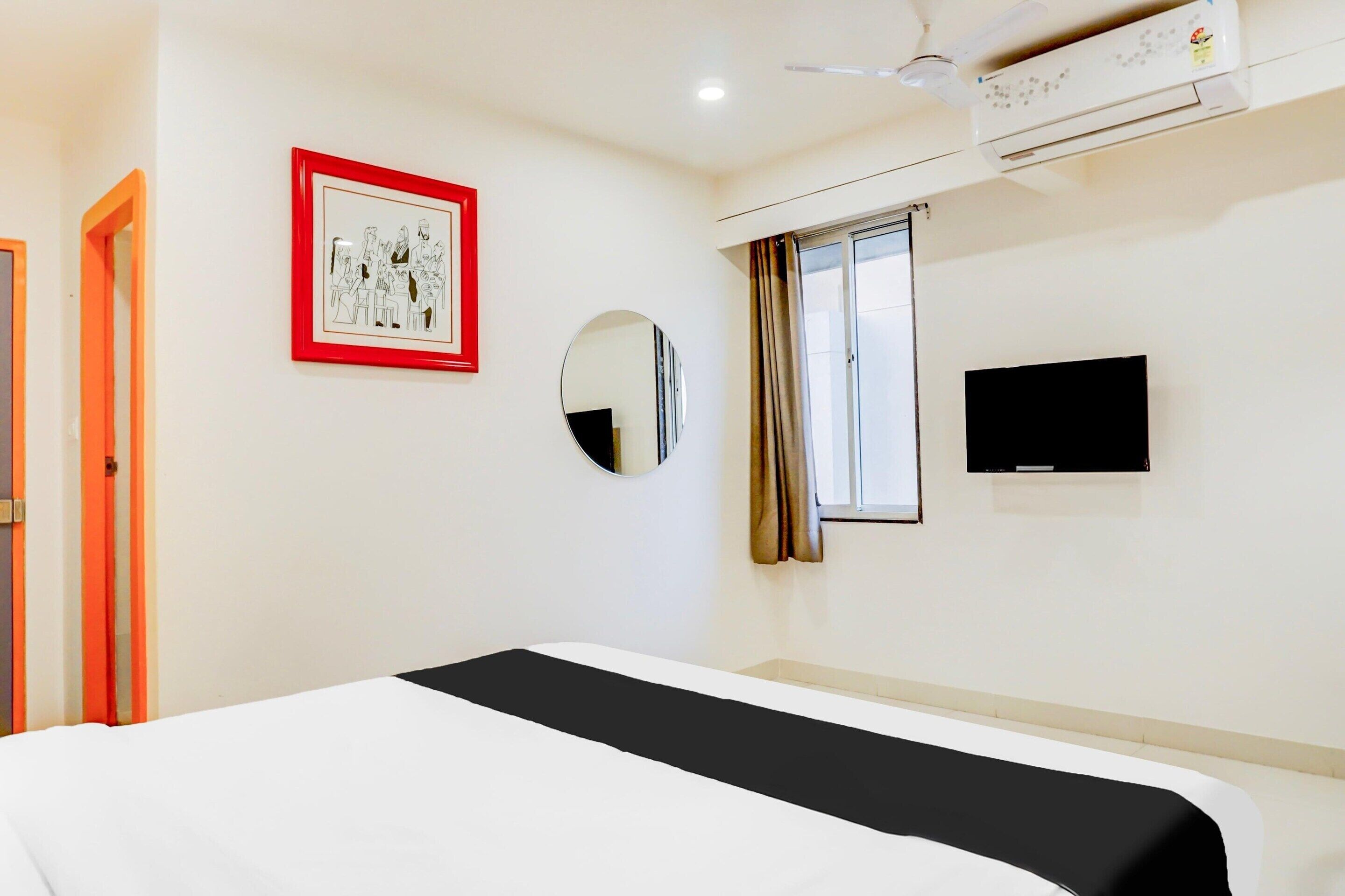 Habitación de hotel con cama, un cuadro enmarcado, espejo, ventana con cortinas, equipo de aire acondicionado y televisor.