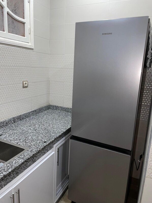 A kitchen with a stainless steel refrigerator, granite countertop, and white tiled backsplash.