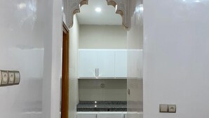 Een smalle gang die uitkomt in een keuken met witte kastjes, een granieten aanrecht en een decoratieve achterwand.