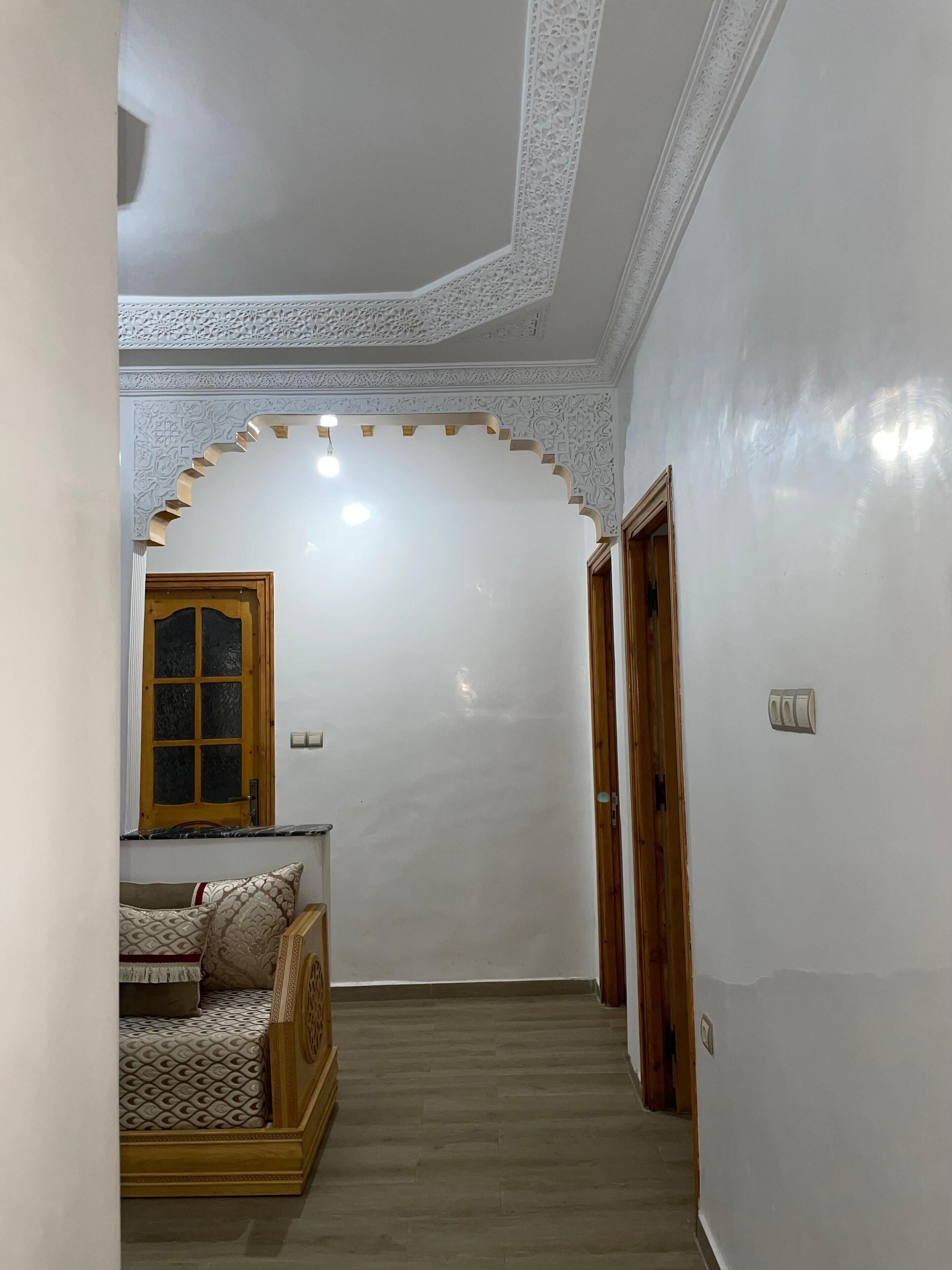 Corredor com cama, porta de madeira e parede branca com design detalhado no teto.