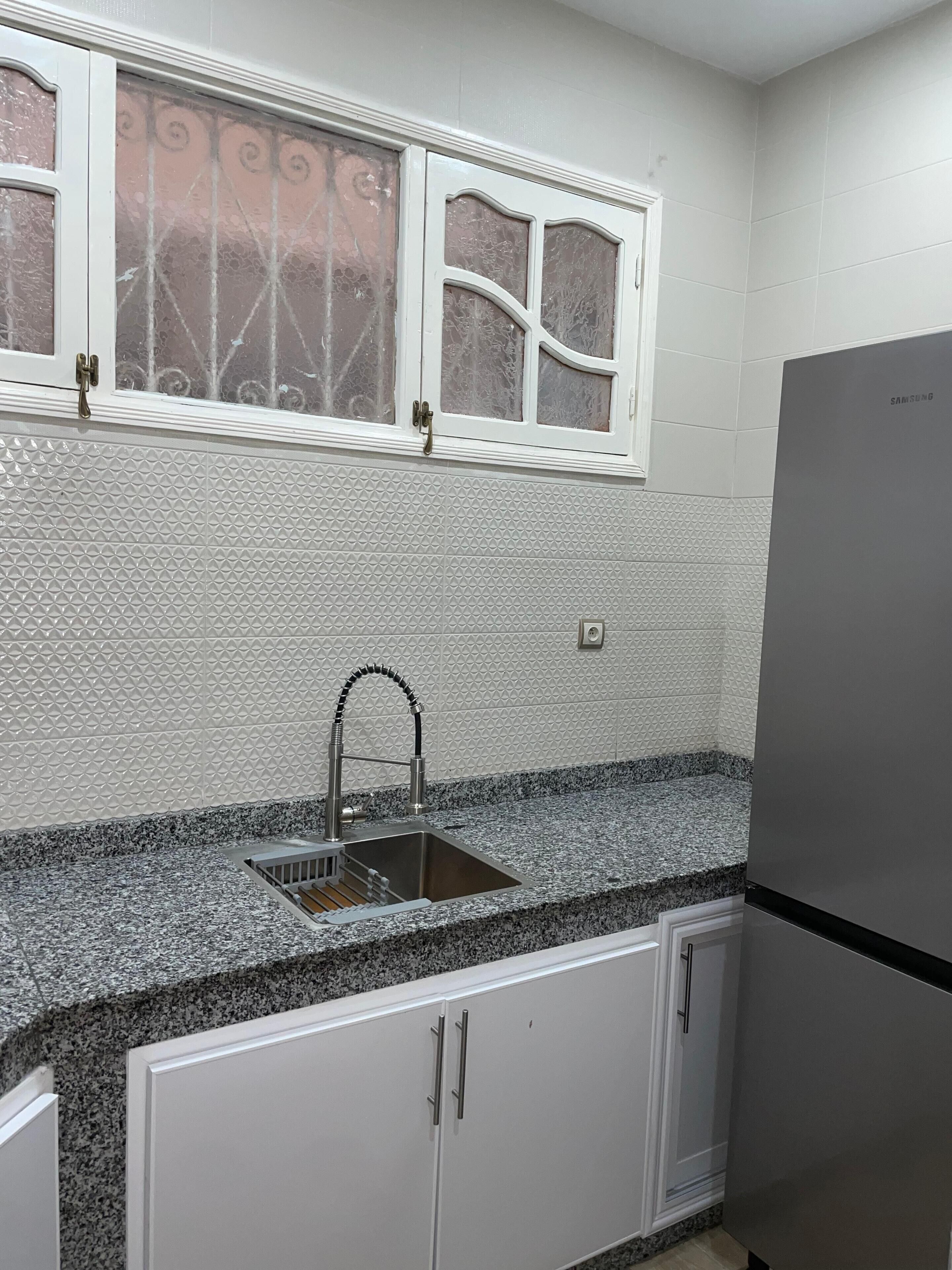 A kitchen with a granite countertop, white cabinets, a stainless steel sink, and a Samsung refrigerator.