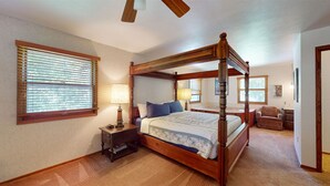 A four-poster bed with a wooden frame, a nightstand with a lamp, a chair, and a small table with a picture frame.
