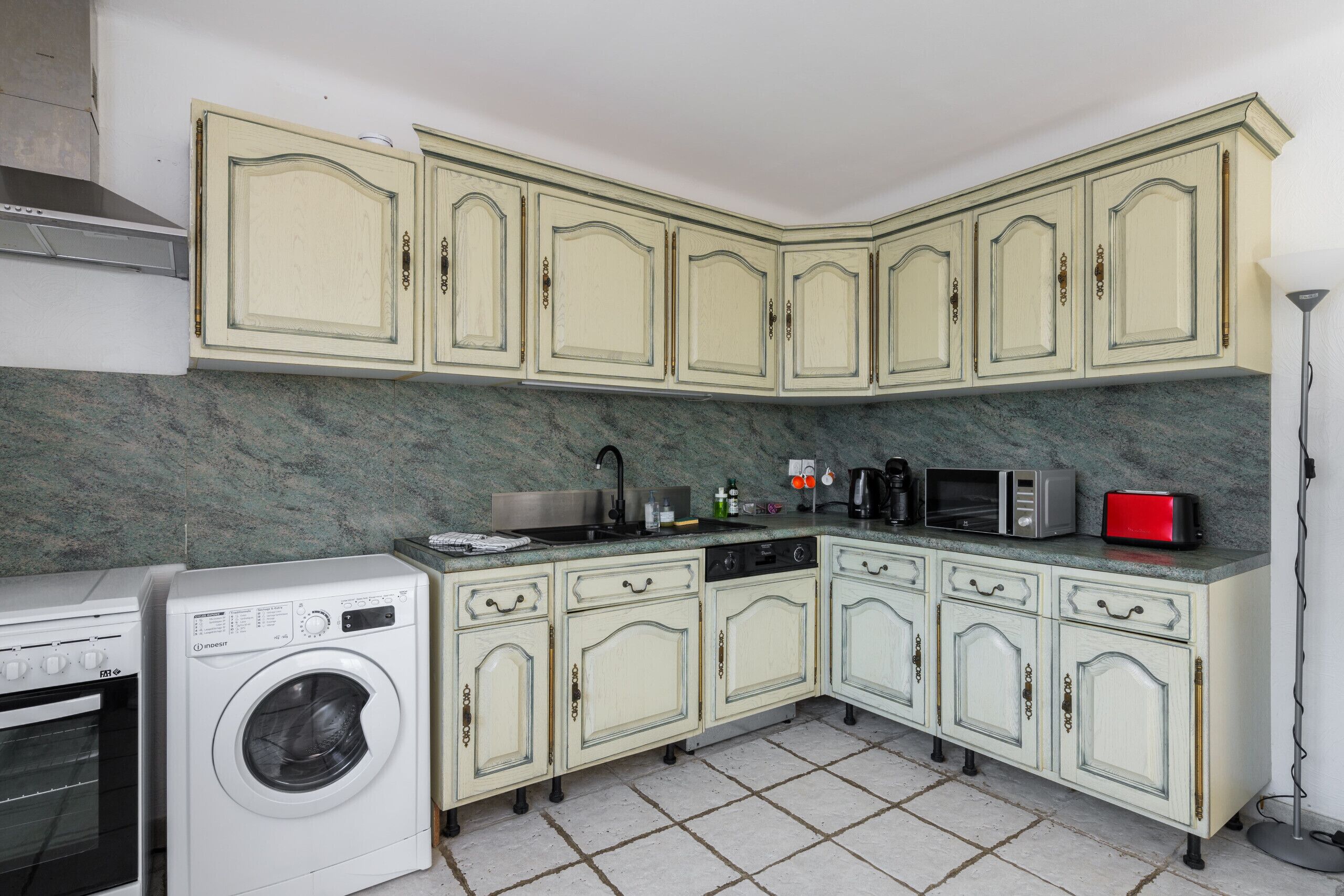 A kitchen with a washing machine, microwave, toaster, and sink.