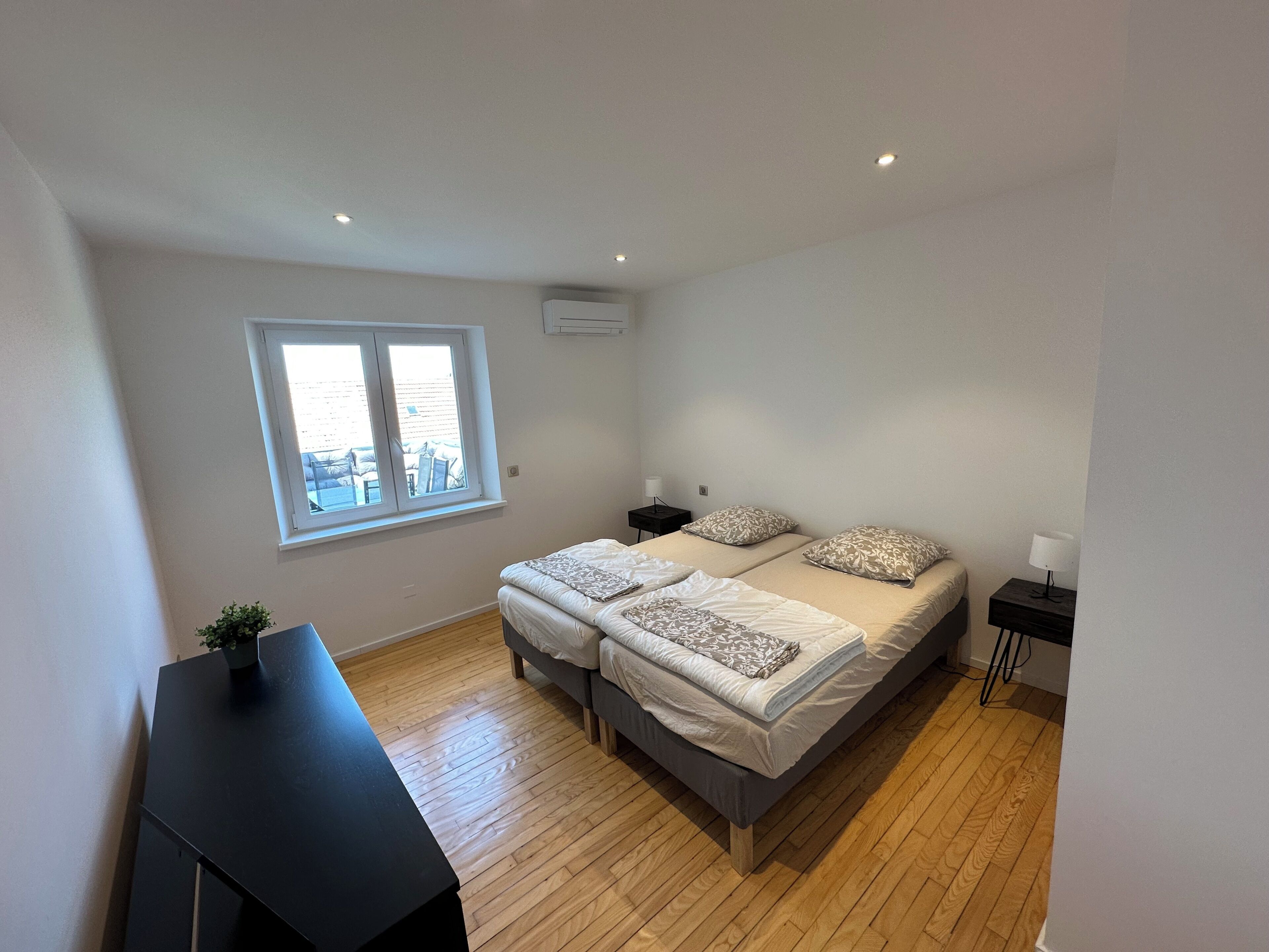 Une chambre moderne avec deux lits, une fenêtre, un bureau et une petite plante.