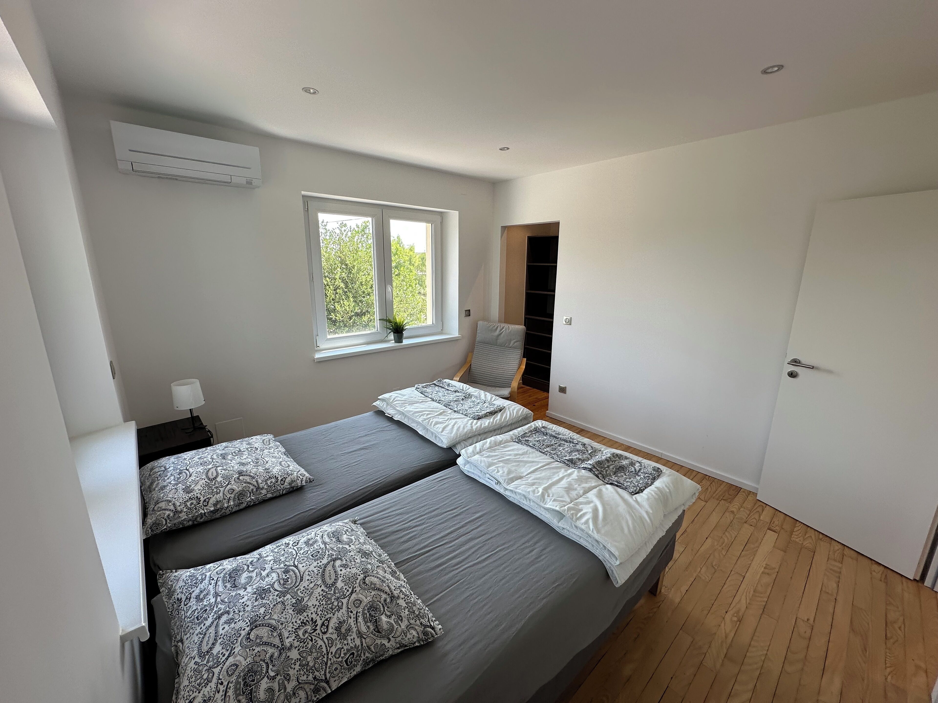A bedroom with two beds, a window with a view, a wardrobe, and a door.