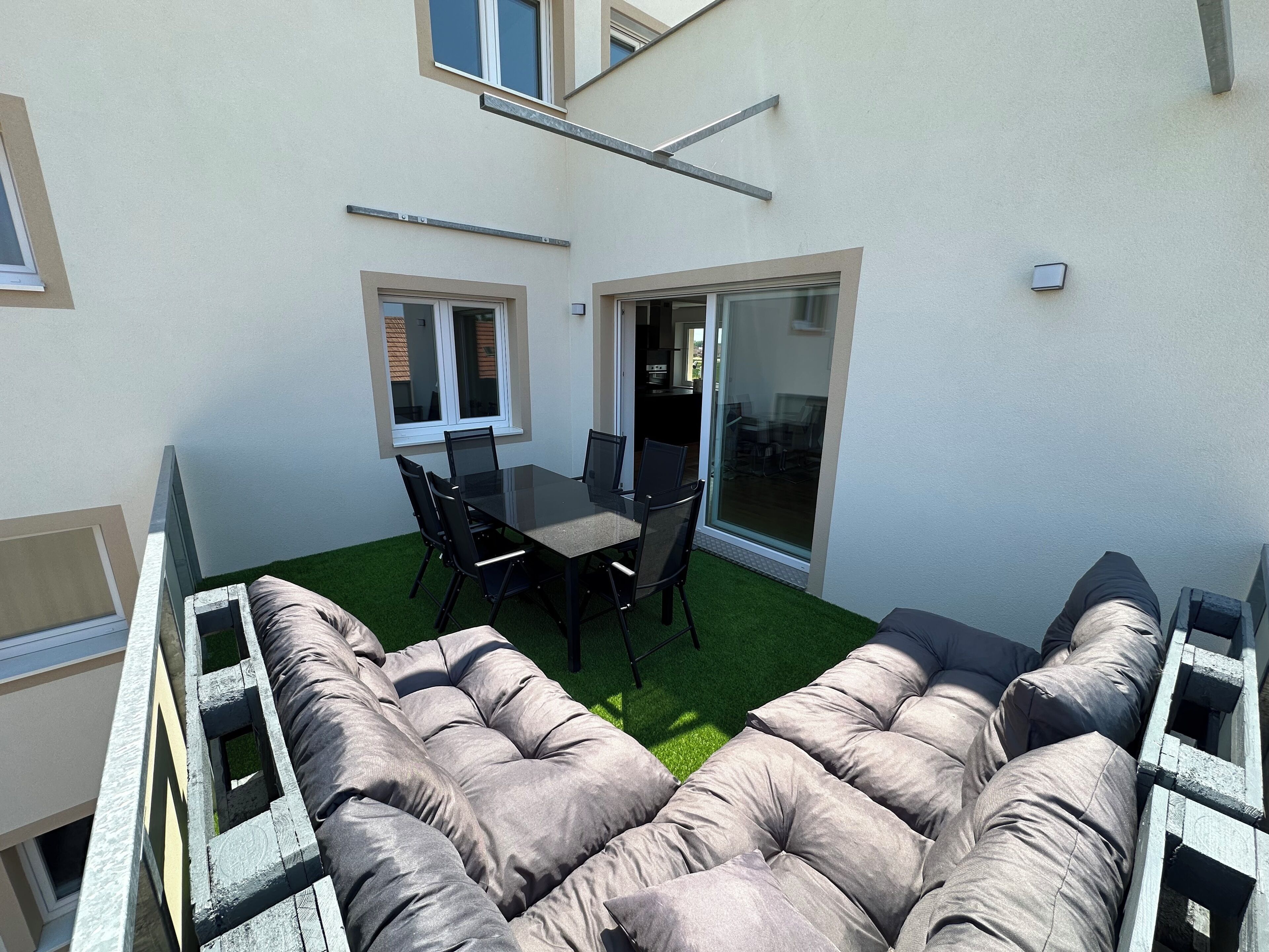 A balcony with a dining table and chairs, a cushioned seating area, and a view of the building's interior.