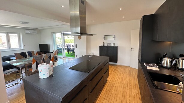 A modern kitchen with a central island, dark cabinetry, and a large window.