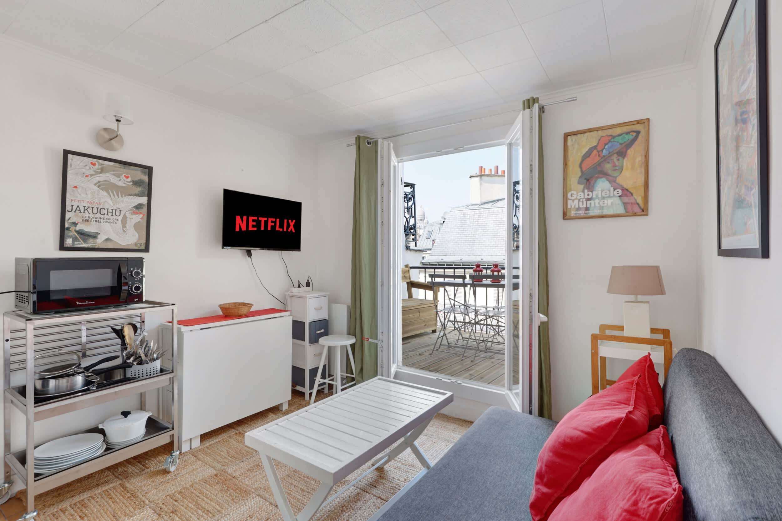 En moderne stue med sofa, fjernsyn, mikrobølgeovn og spiseplads med bord og stole.