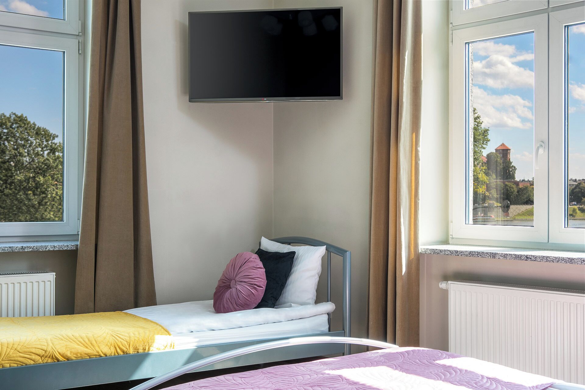 Une chambre avec deux lits simples, un téléviseur fixé au mur et une fenêtre donnant sur un château.