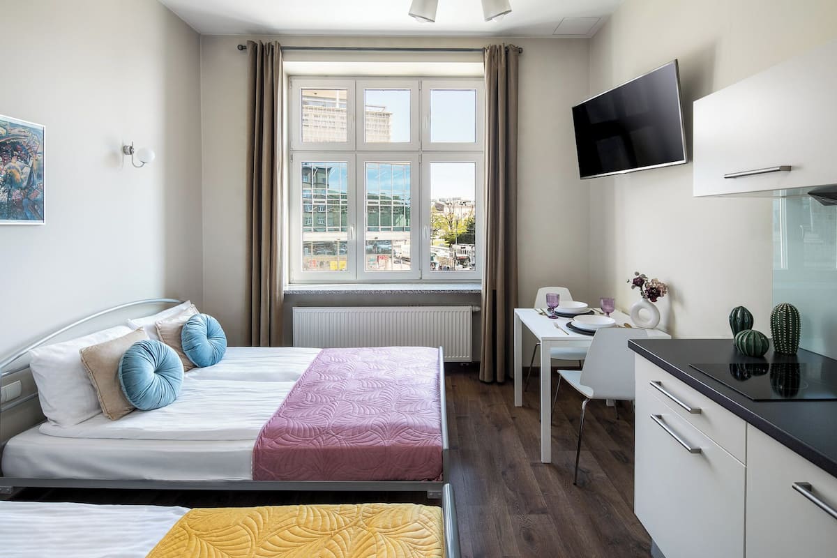 A hotel room with two beds, a desk, a TV, and a view of the city.