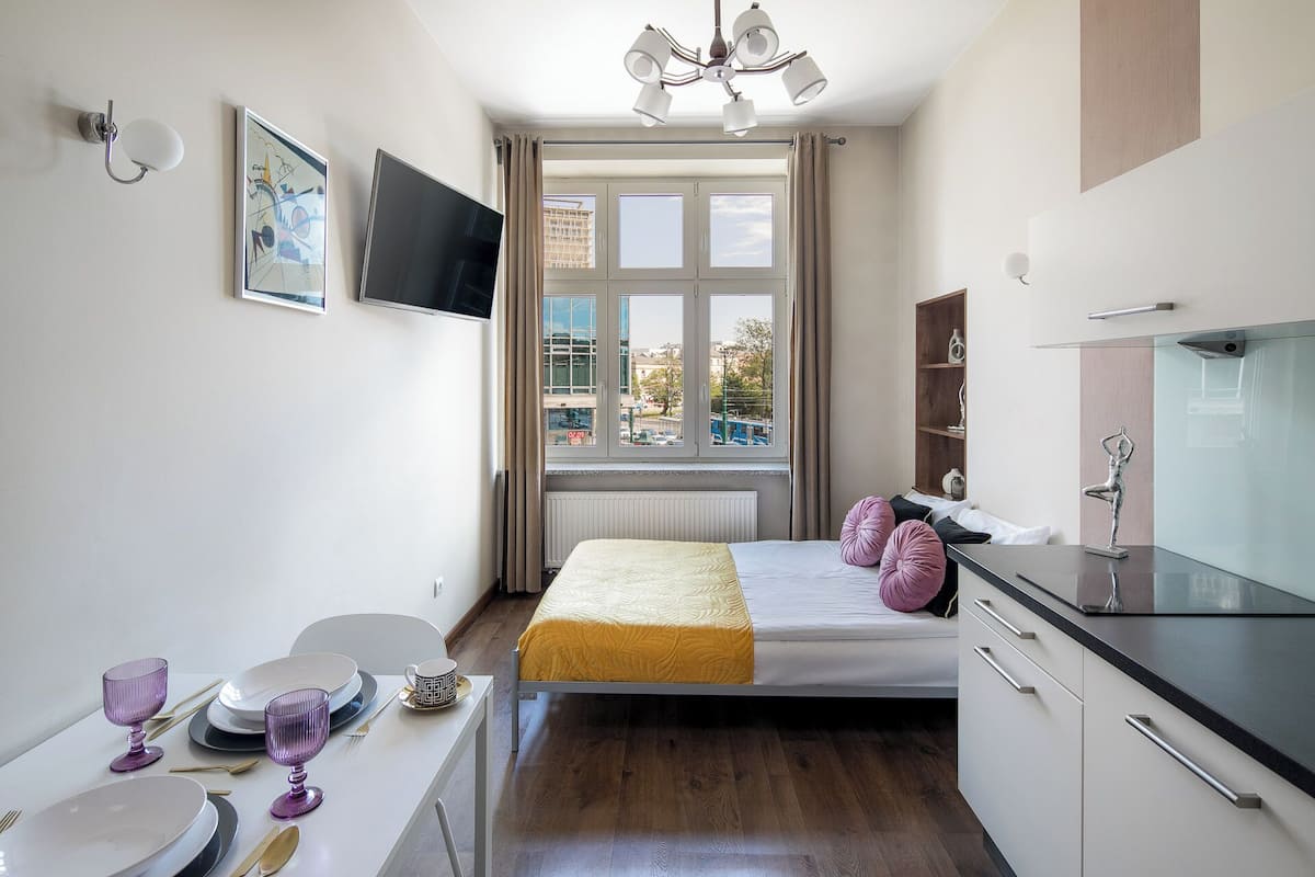 A modern bedroom with a bed, bedside table, TV, and a window with a city view.