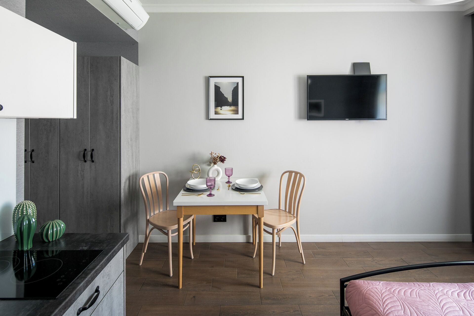 Een moderne keuken met een eethoek, met een witte tafel, twee houten stoelen en een zwarte televisie aan de muur.