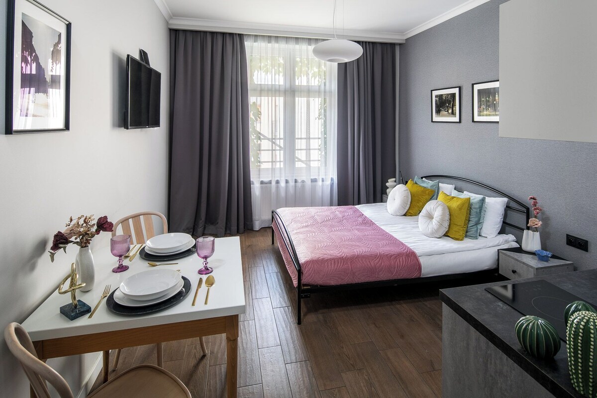 A modern hotel room with a bed, bedside table, and a dining area with a table set for two.